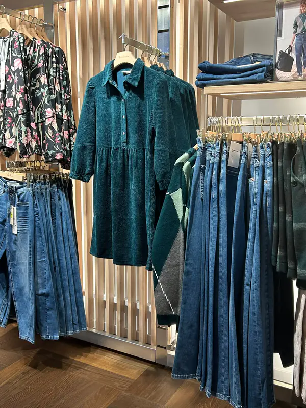 Robe en velours canard et chemisier fleuri, devant le mur de jeans
